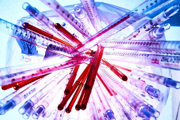 Eine Wissenschaftlerin und ein Wissenschaftler arbeiten hinter einer Glasfassade und mischen Chemikalien mit Großgeräten.